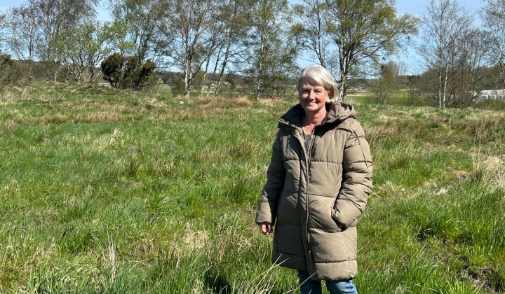 Britt-Marie Johannsson står på en bit gräsbevuxen mark där de i framtiden tänkt bygga en maskinhall.
