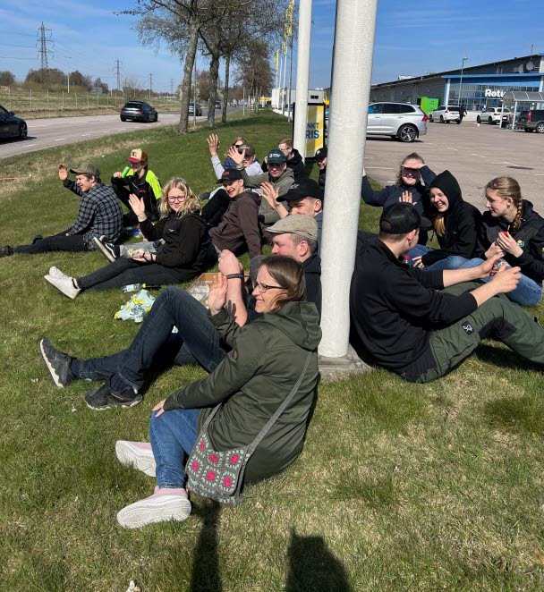Personer sitter vid flaggstänger på en gräsmatta i stadsmiljö
