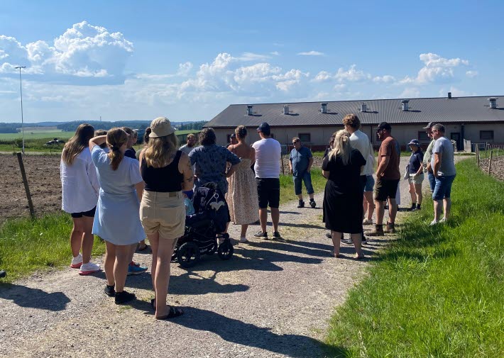 Deltagare på generationsskiftesträff går en rundvandring på en grusväg. i bilden ses också ett svinhus.