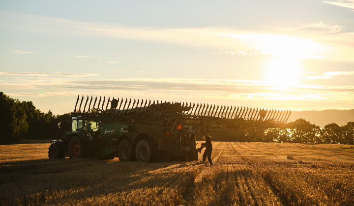 Traktor med gödseltunna och bonde i motljus